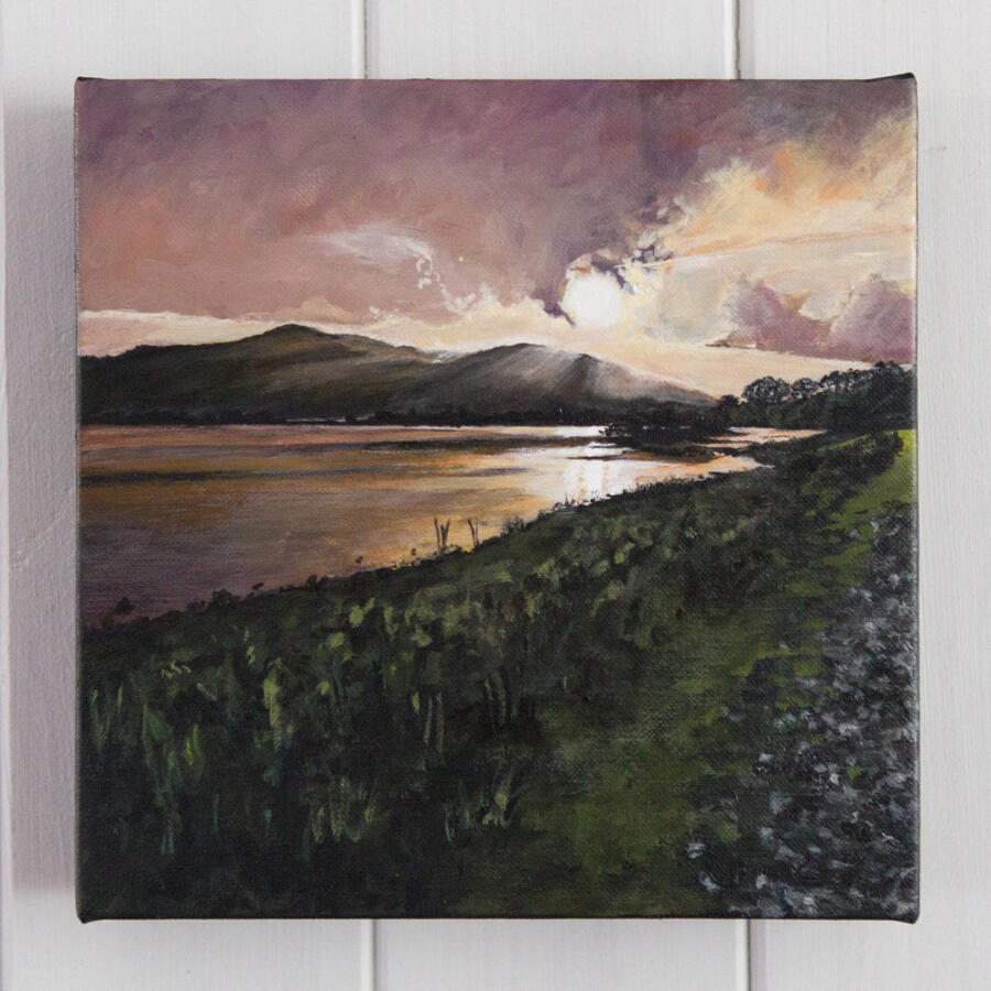 Landscape painting of a golden sunset over a calm reflective lake, with rolling dark hills in the distance, a glowing purple-orange sky, and a grassy shoreline path leading along the water’s edge.